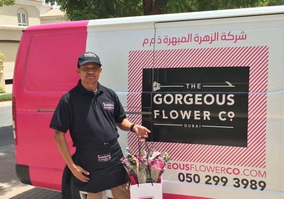 Smiling delivery driver with flower delivery besides branded van